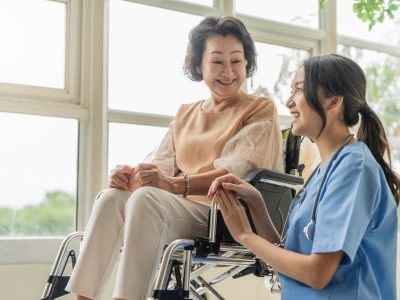 asian young caregiver caring for her elderly patient at senior daycare Handicap patient in a wheelchair at the hospital talking to a friendly nurse and looking cheerful nurse wheeling Senior patient