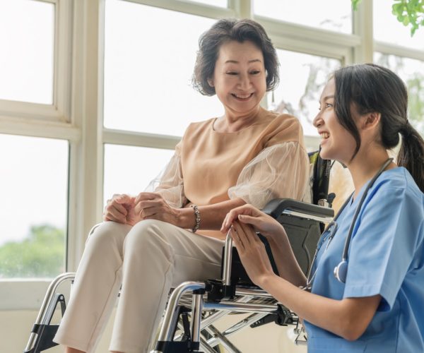 asian young caregiver caring for her elderly patient at senior daycare Handicap patient in a wheelchair at the hospital talking to a friendly nurse and looking cheerful nurse wheeling Senior patient